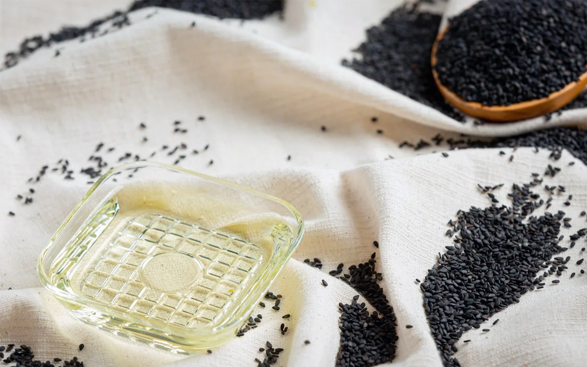 An image featuring black sesame seeds and a glass of oil, emphasizing their benefits for skin, weight, and overall health.