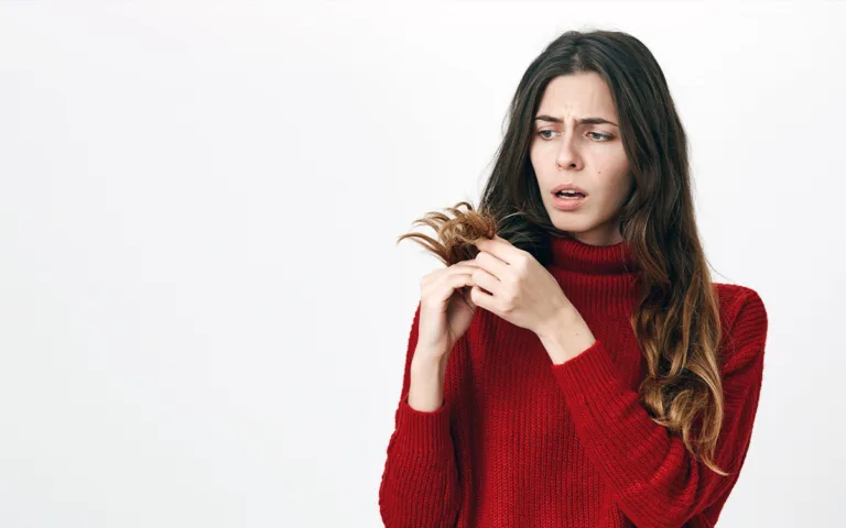 A woman in a red sweater gently combs her hair, showcasing a focus on hair care and managing frizz effectively.