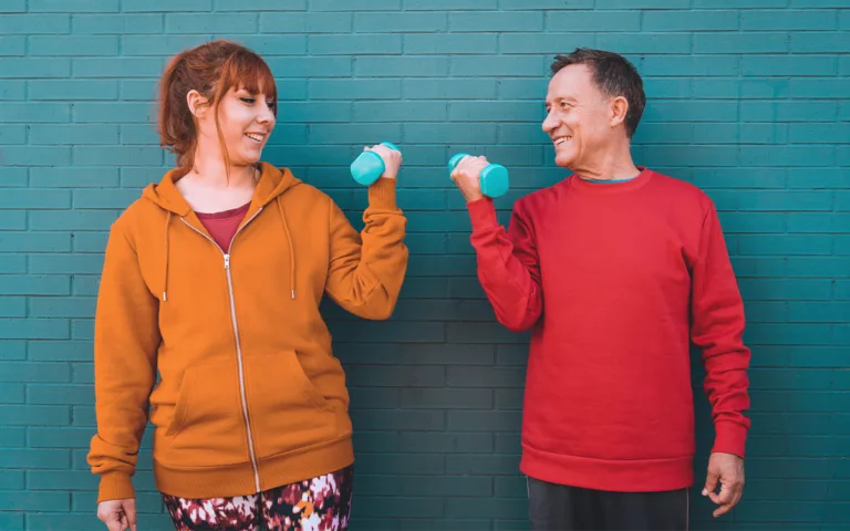 A man and woman exercise with dumbbells, representing the connection between movement and a happier mindset.