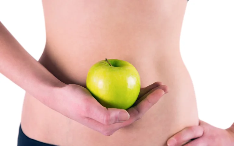 A woman with an apple in hand, representing the importance of nutrient-rich foods for a flat belly and overall health.