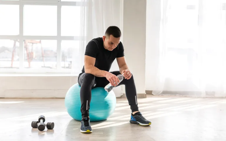 A man on an exercise ball with a water bottle, highlighting the importance of hydration and nutrition in muscle recovery.