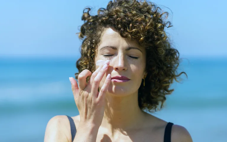 A woman with curly hair is seen applying sunscreen, highlighting the significance of daily SPF use for healthy skin.