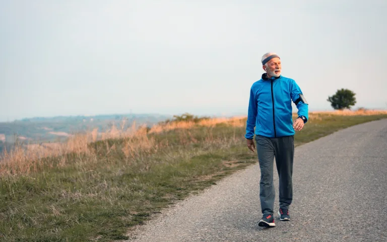 An older man walking on a road, promoting daily walks for health benefits like improved blood pressure and joint flexibility.
