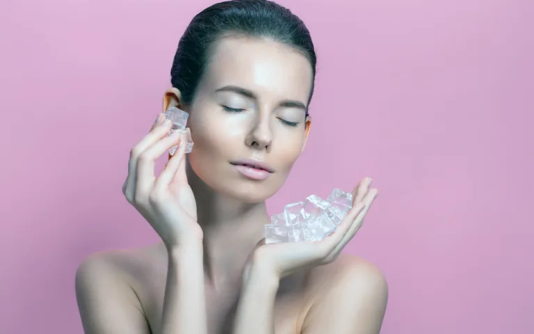 A stunning woman with ice on a pink backdrop, highlighting the benefits of ice-rolling for radiant skin.
