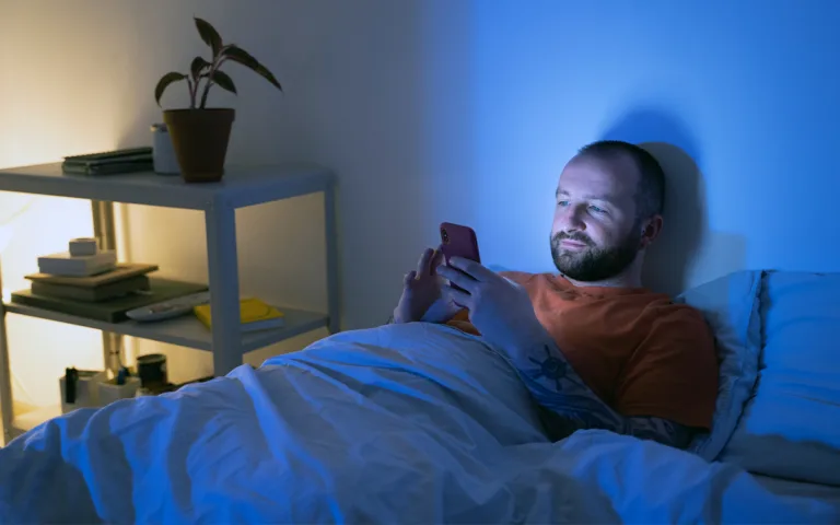 A man in bed holding his phone, highlighting the impact of blue light on sleep and circadian rhythm.