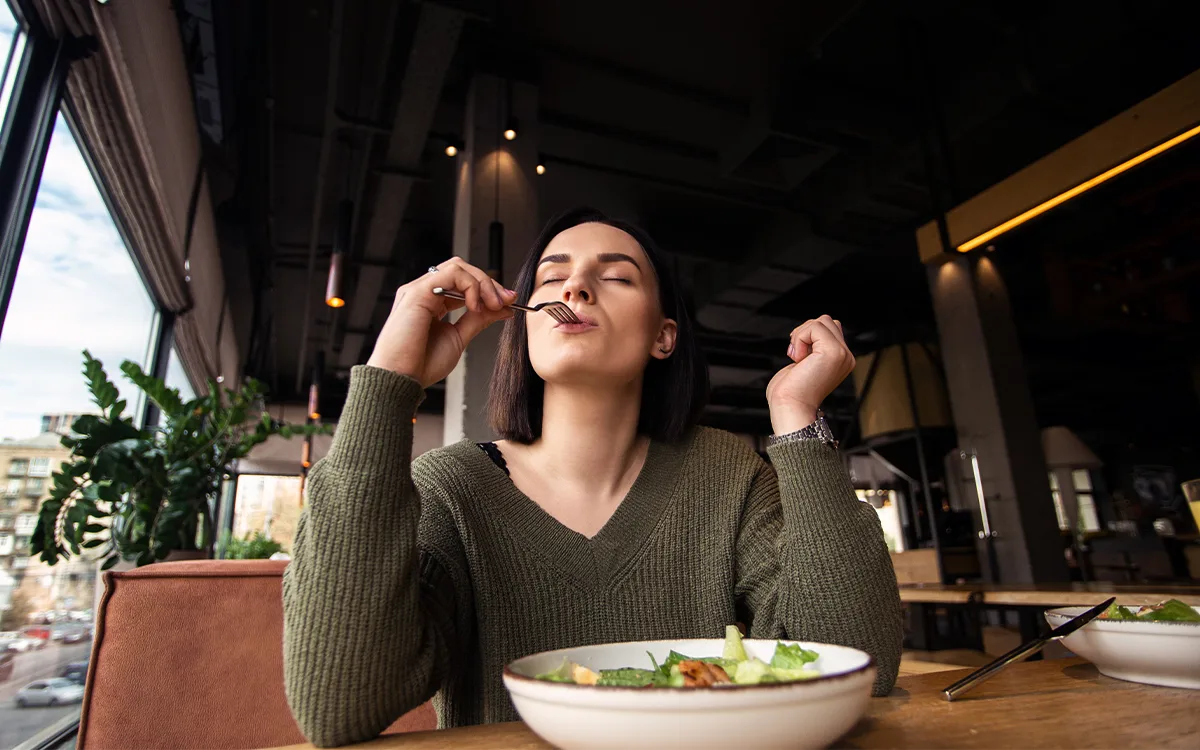 A woman dining on a colorful salad in a restaurant, emphasizing the link between healthy eating and improved mood.