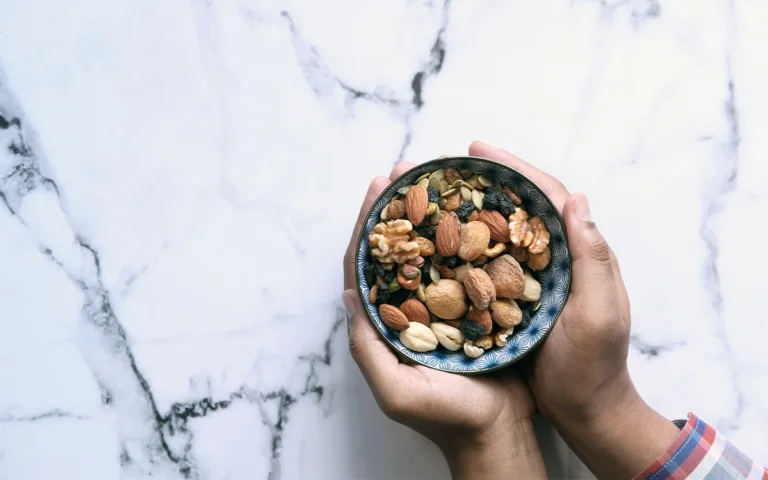 A cheerful woman presents a bowl of nuts on a marble countertop, emphasizing the health benefits of proper nut intake.