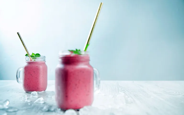 Two mason jars containing pink smoothie rest on a wooden table, highlighting a delicious and health-conscious drink choice.
