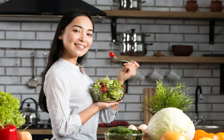 A woman in a kitchen holds a bowl of salad, exploring ways to enhance satisfaction with healthy ingredients.