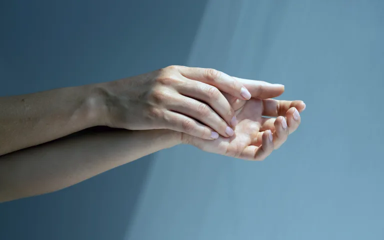 A person shielding their face with their hand, highlighting the importance of skincare for hands and face against aging.