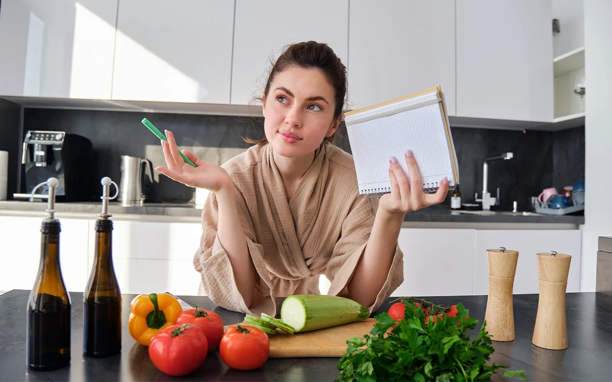 A woman sitting at a kitchen table holds a clipboard, ready to discuss nutrition myths and healthy food choices.