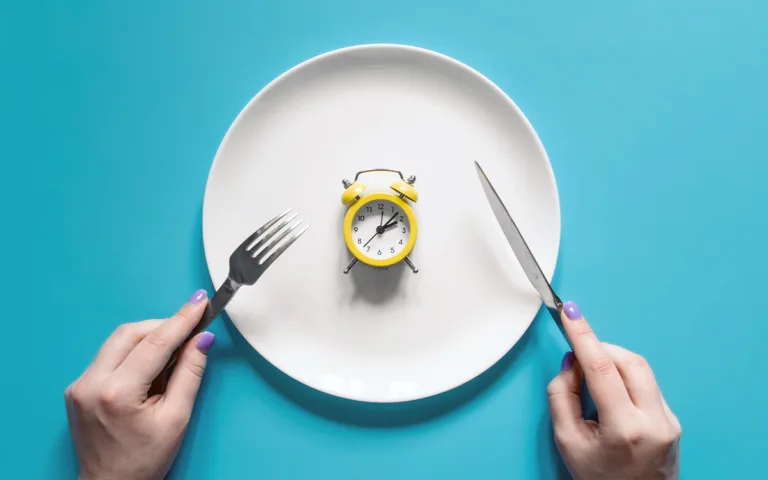 A person holds a fork and knife over a plate featuring a clock, symbolizing the connection between eating and circadian rhythms.