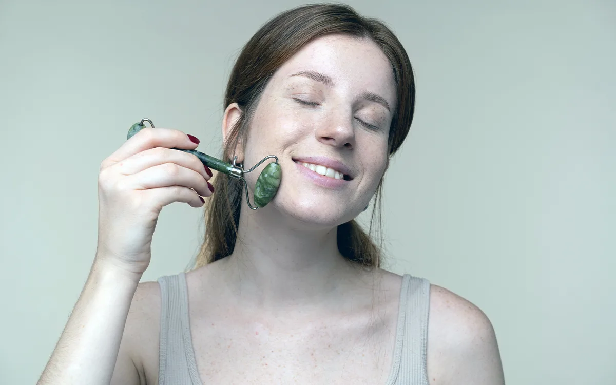 A woman brushes her face while using a jade roller for skincare.