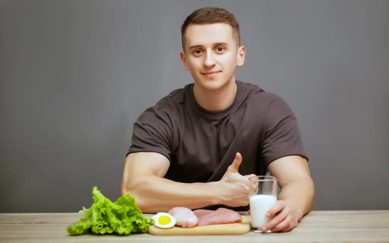 A man sits at a table with a glass of milk and a plate of nutritious food, focusing on muscle-building nutrition.