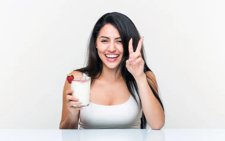 A woman holds a glass of Greek yogurt, representing a healthy lifestyle and the importance of nutrition for hair care.