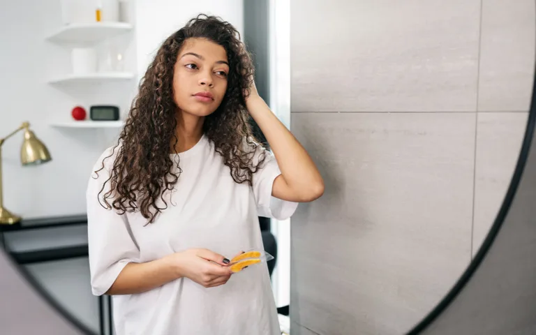 A woman with curly hair stands in front of a mirror, reflecting on hair care and porosity for better hydration.