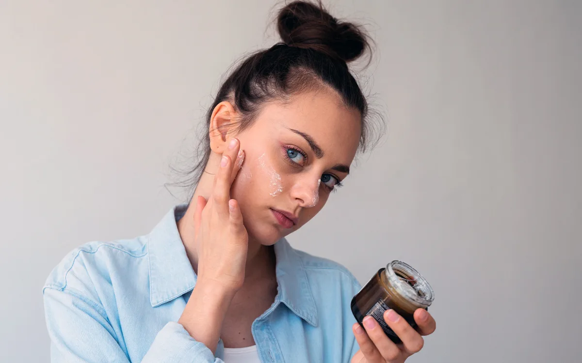 A woman holds a jar of face cream, showcasing the benefits of waterless skincare for enhanced beauty and eco-friendliness.