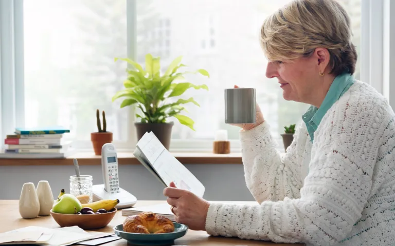 A woman sits at a table with a cup of coffee and a tablet, reflecting on simple habits for a healthier life.