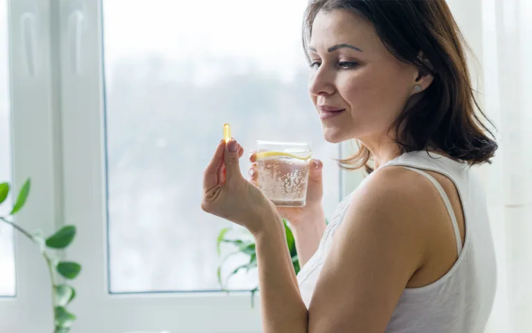 A woman holds a glass of water and a pill, symbolizing the importance of magnesium supplements for health and wellness.