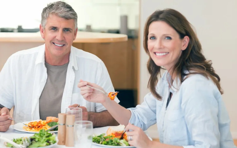 A man and woman enjoy a healthy salad at a table, reflecting on lifestyle changes and nutritional needs after turning 40.