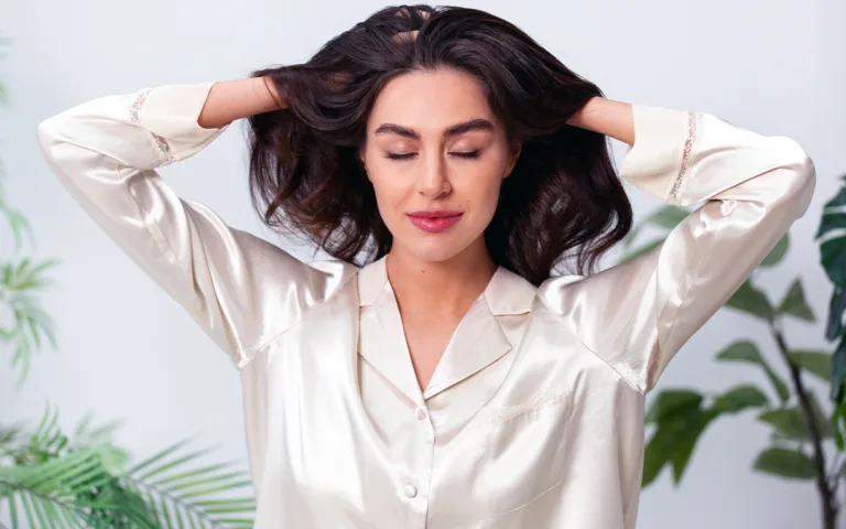 A woman in a white shirt gently touches her hair, showcasing its healthy, glossy appearance.
