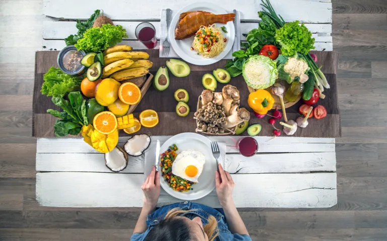 Top view of a woman enjoying a colorful, healthy meal on a wooden table, highlighting nutritious food choices.