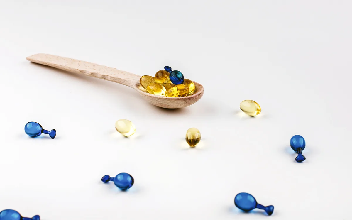 A wooden spoon holds blue and yellow fish oil capsules, highlighting their potential health benefits for immune support and bones.