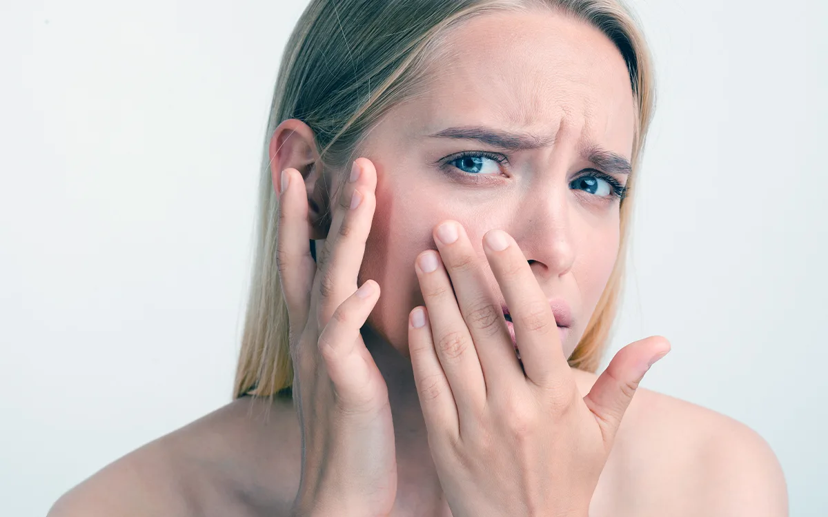 A woman with her hands on her face, expressing concern about summer breakouts and skincare challenges.