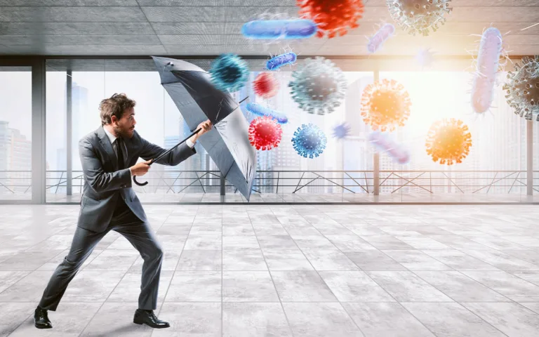 Businessman holding an umbrella over a virus, symbolizing protection and the immune system's broader roles in health.