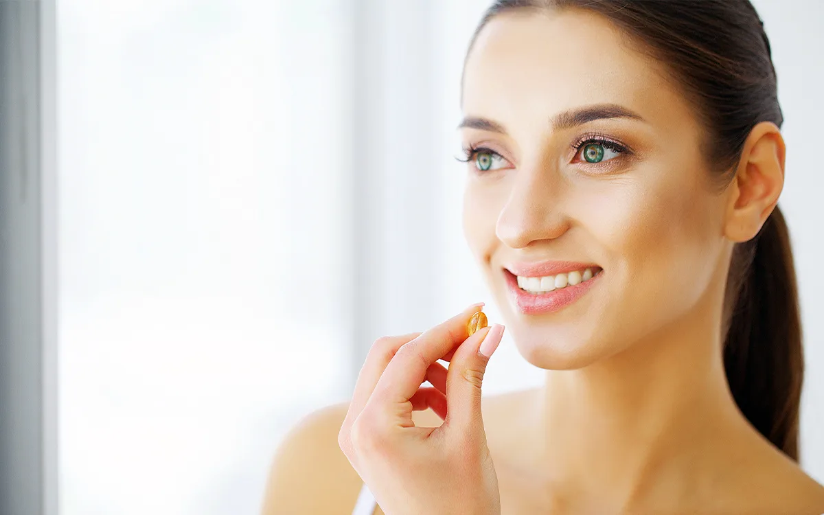 A woman smiles while holding supplement, emphasizing the role of dietary supplements in achieving glowing skin and health.