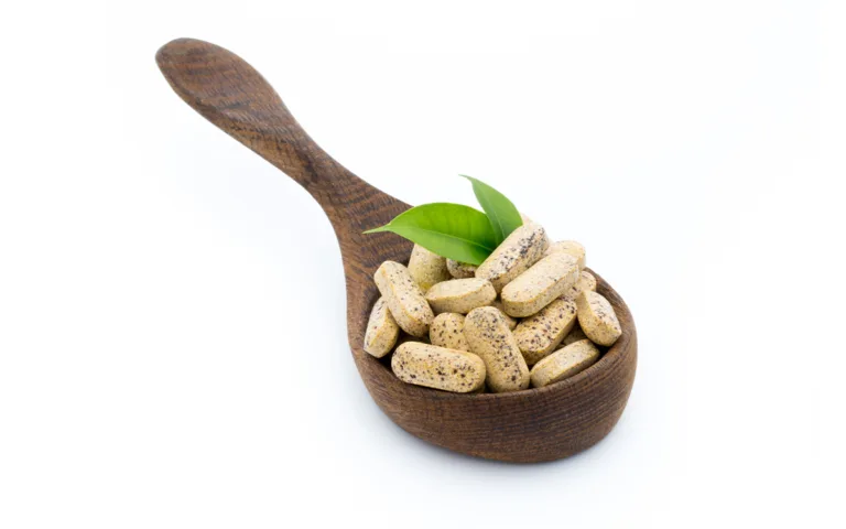 A wooden spoon holds various pills and green leaves, symbolizing daily fiber supplements for digestive health.