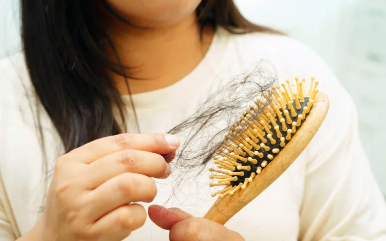 A woman holding a hair brush, reflecting on her hair's health and potential signs of nutritional deficiencies or stress.