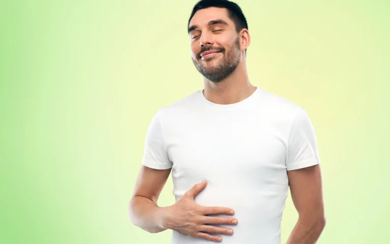 A man wearing a white t-shirt clutches his stomach, indicating feelings of bloating or sluggishness in his digestive system.