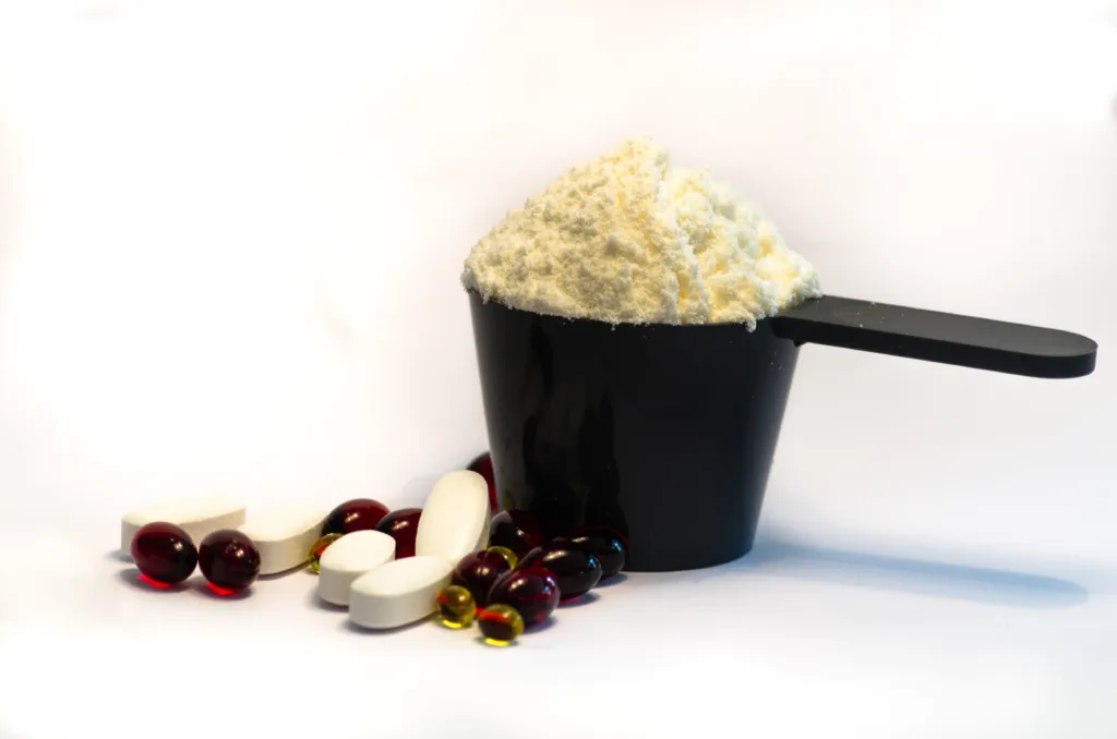  A black cup containing a scoop of powder and several pills, representing Vitamin D3 and K2 supplements for daily nutrition.