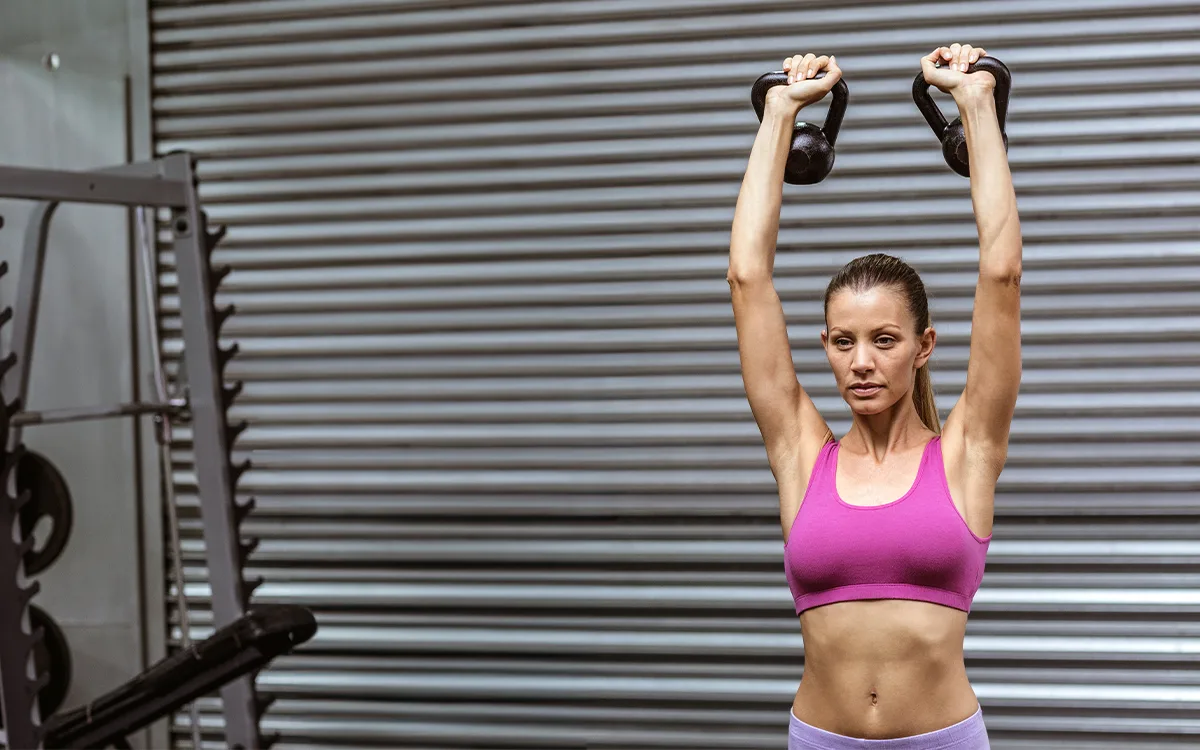 A woman in a pink top holds a kettlebell, demonstrating strength training for women of all ages to enhance fitness and health.