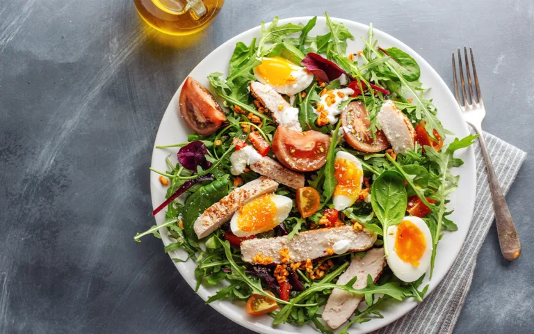 A plate featuring a cooked egg, grilled chicken, and a variety of colorful vegetables, promoting a healthy diet.