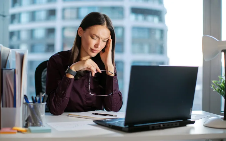 A tired woman working at a desk with a laptop, exploring common causes of low energy and ways to boost health naturally.