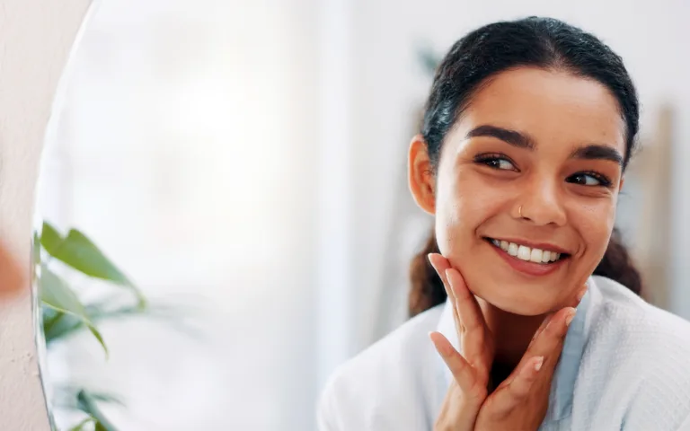 A woman smiles at her reflection in the mirror, highlighting her glowing skin and confidence during her weight management journey.