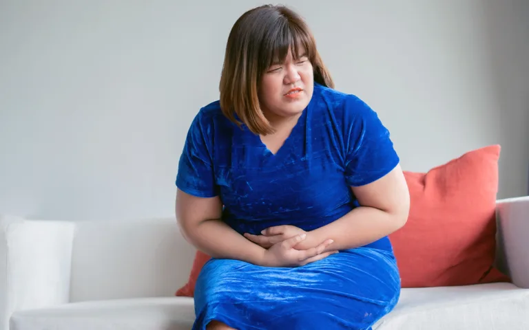 A woman sits on a couch, holding her stomach in discomfort, reflecting the common menopause symptom of bloating.