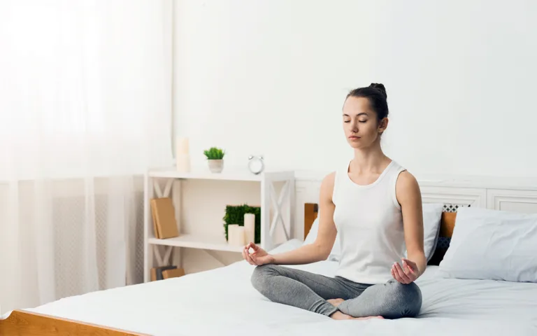 A woman practices yoga on a bed in a serene room, promoting relaxation and mindfulness for better sleep.