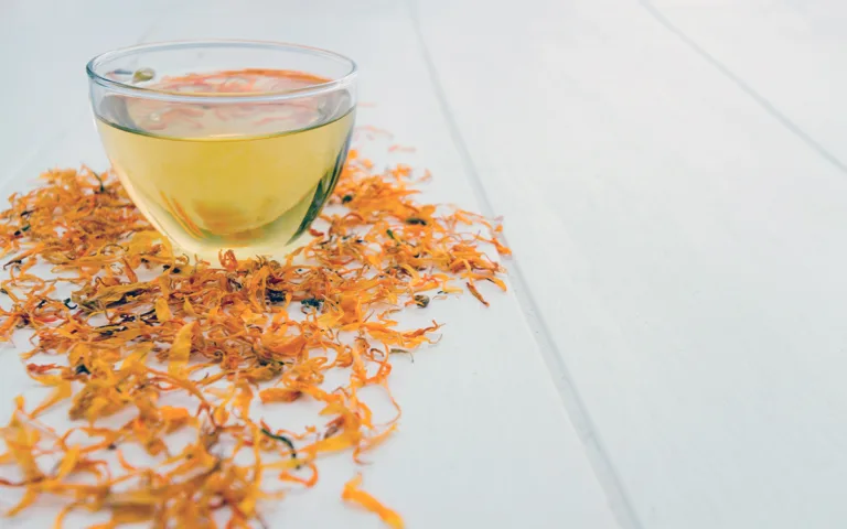 A glass of tea beside dried flowers on a table, suggesting a calming and natural atmosphere.