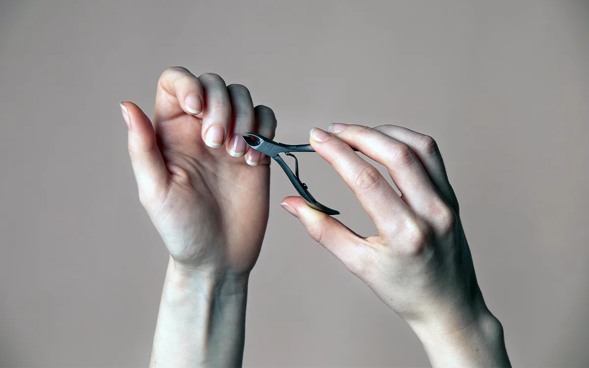 A pair of hands holding scissors, ready for nail grooming or trimming, emphasizing nail health and care.