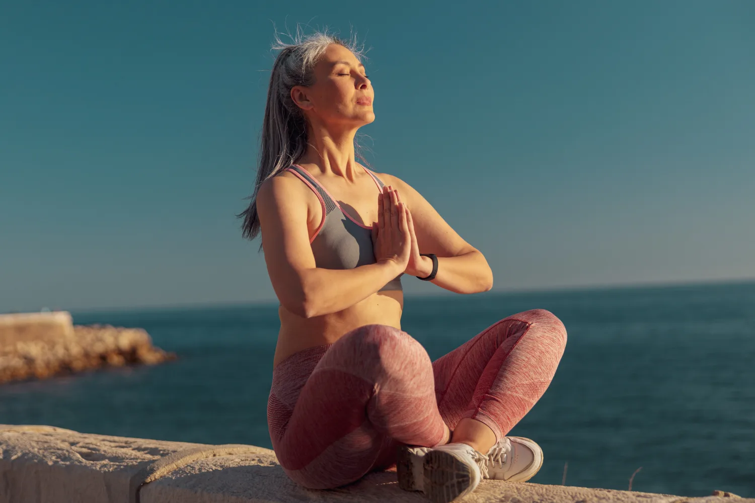 Woman practicing mindful breathing and meditation by the sea, a daily habit that supports stress reduction and healthy cortisol balance during menopause