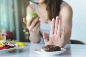 Person choosing an apple over a chocolate donut, representing healthier food choices and reduced sugar cravings through better glucose control.