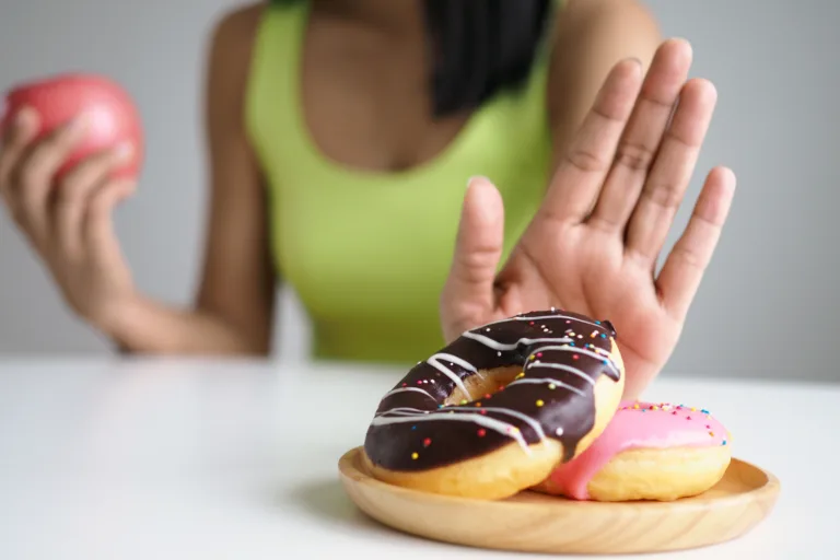 Woman refusing donuts while holding fruit, illustrating avoiding sugary foods to manage menopause symptoms and maintain hormone balance.