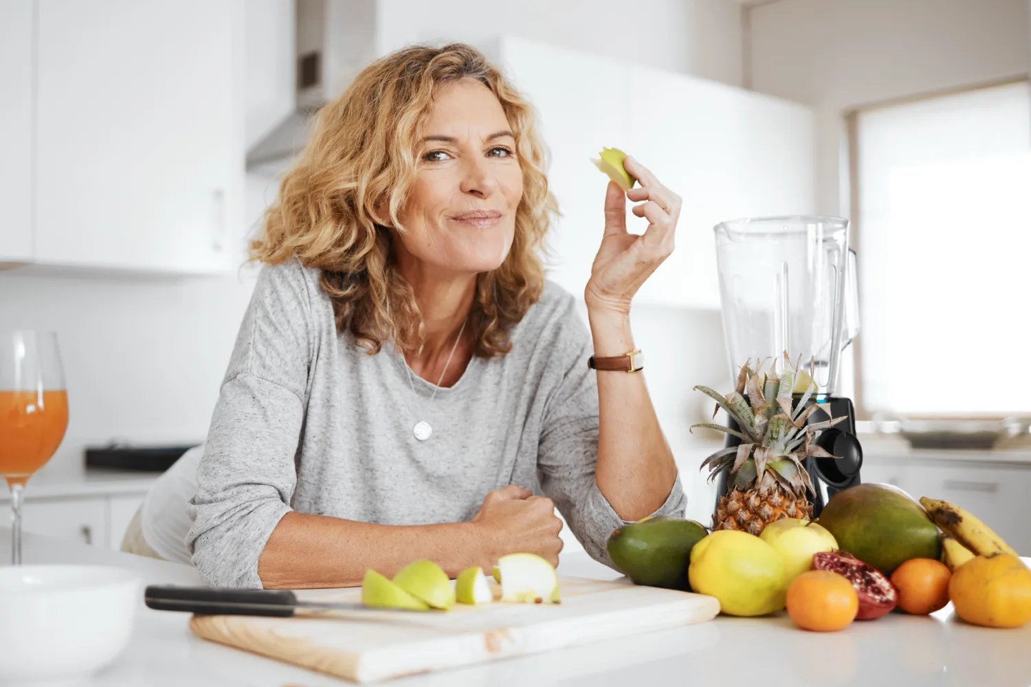 Woman eating fresh fruits in kitchen, symbolizing healthy eating habits that support hormone balance and reduce menopause symptoms naturally.
