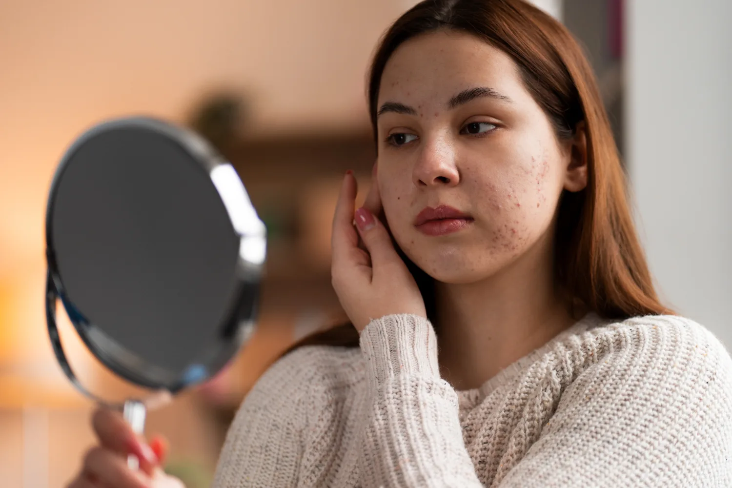 Young woman looking in mirror noticing acne and skin problems that may be linked to poor sleep habits affecting skin health and aging