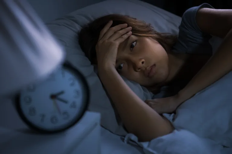 Woman lying awake in bed at night struggling with insomnia and poor sleep habits that can increase stress and contribute to premature skin aging