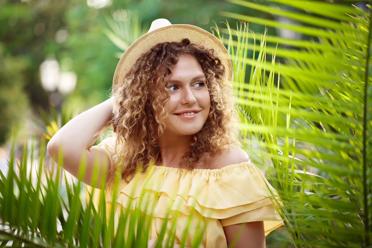 Smiling woman with curly hair wearing hat outdoors representing healthy scalp, improved hair thickness and nutrition supported hair care