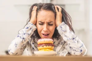 Woman stressed while looking at donuts showing food cravings and food noise linked to emotional stress and unhealthy eating habits